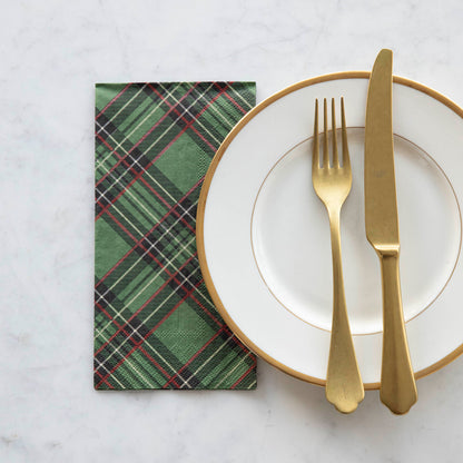 A square cocktail napkin featuring a diagonal plaid pattern of black, red and white over medium green.