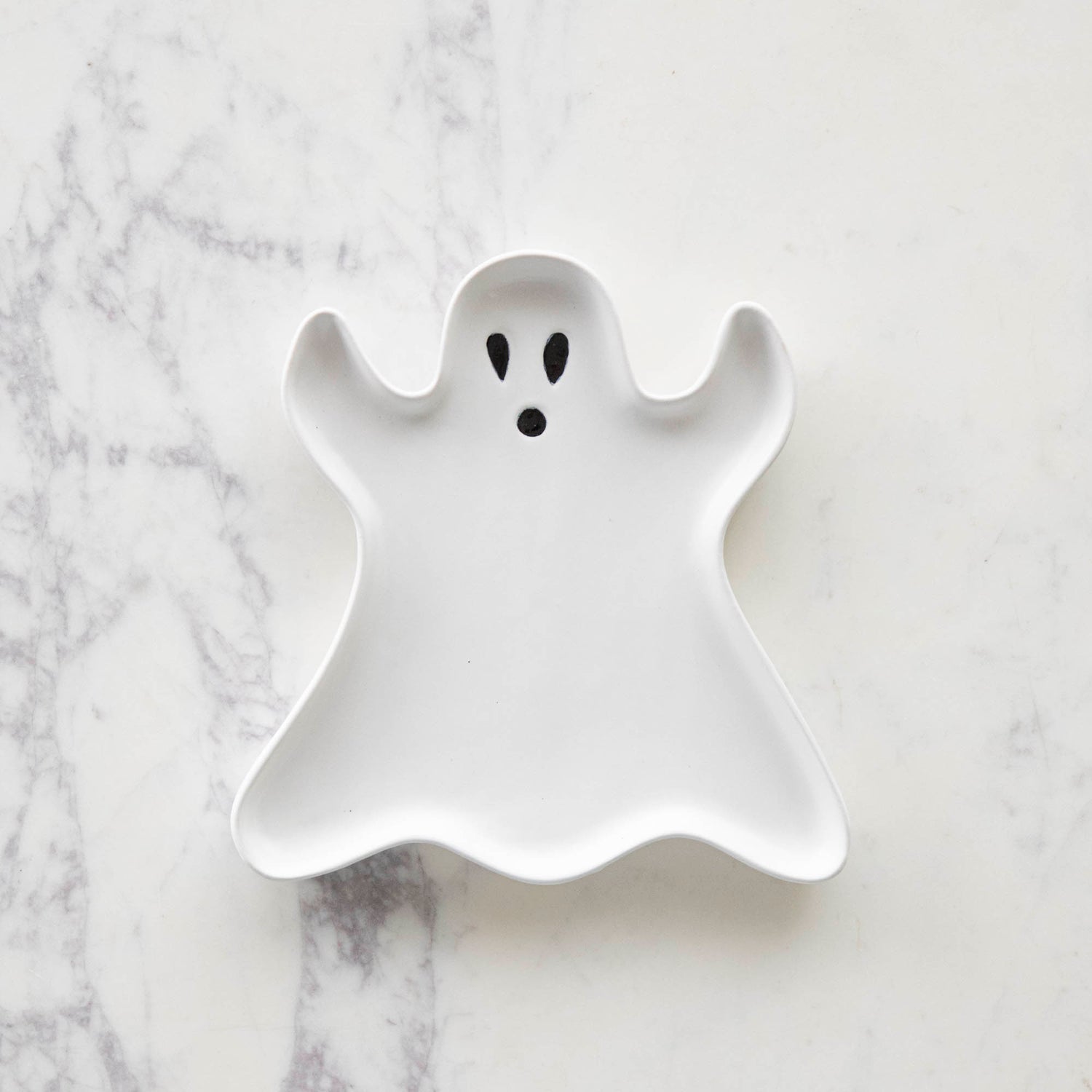 Stoneware Ghost Shaped Plate with black teardrop eyes and a black circular mouth, on a marble table.