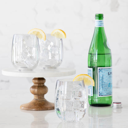 3 Clear SymGlasses with lemon wedges on the rim and bottle of water in background