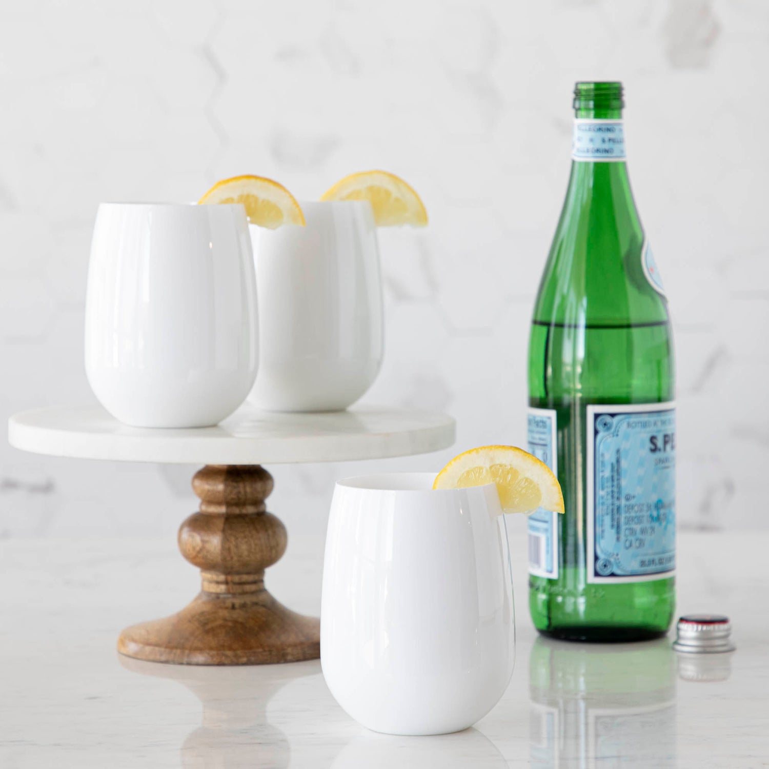 3 white Symglasses with lemon wedges and bottle of water in background