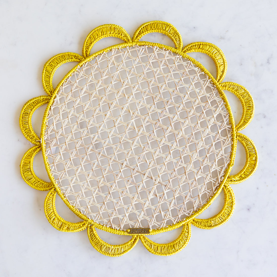 Iraca palm woven placemat with a neutral center and yellow scallops along the edge. 
