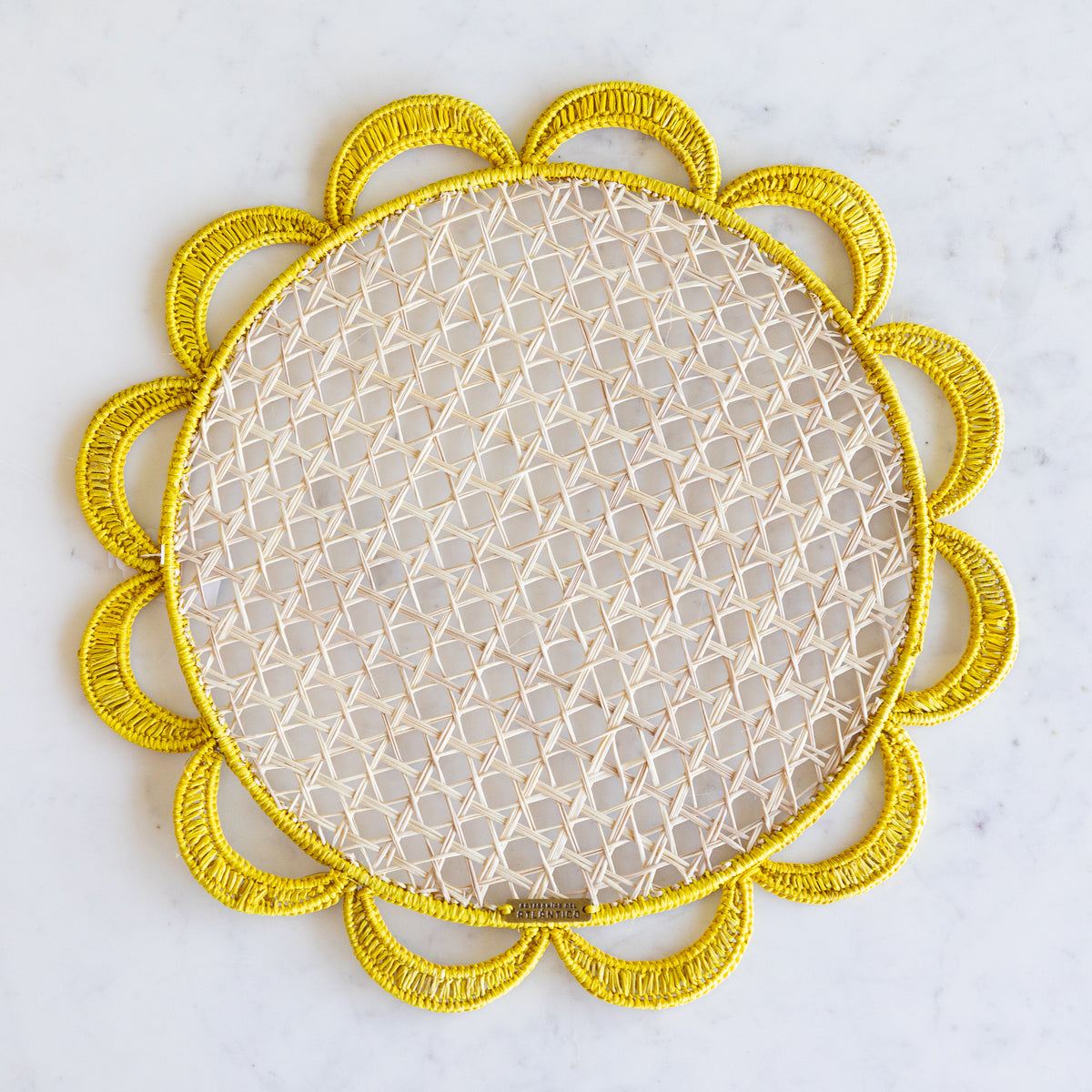 Iraca palm woven placemat with a neutral center and yellow scallops along the edge. 
