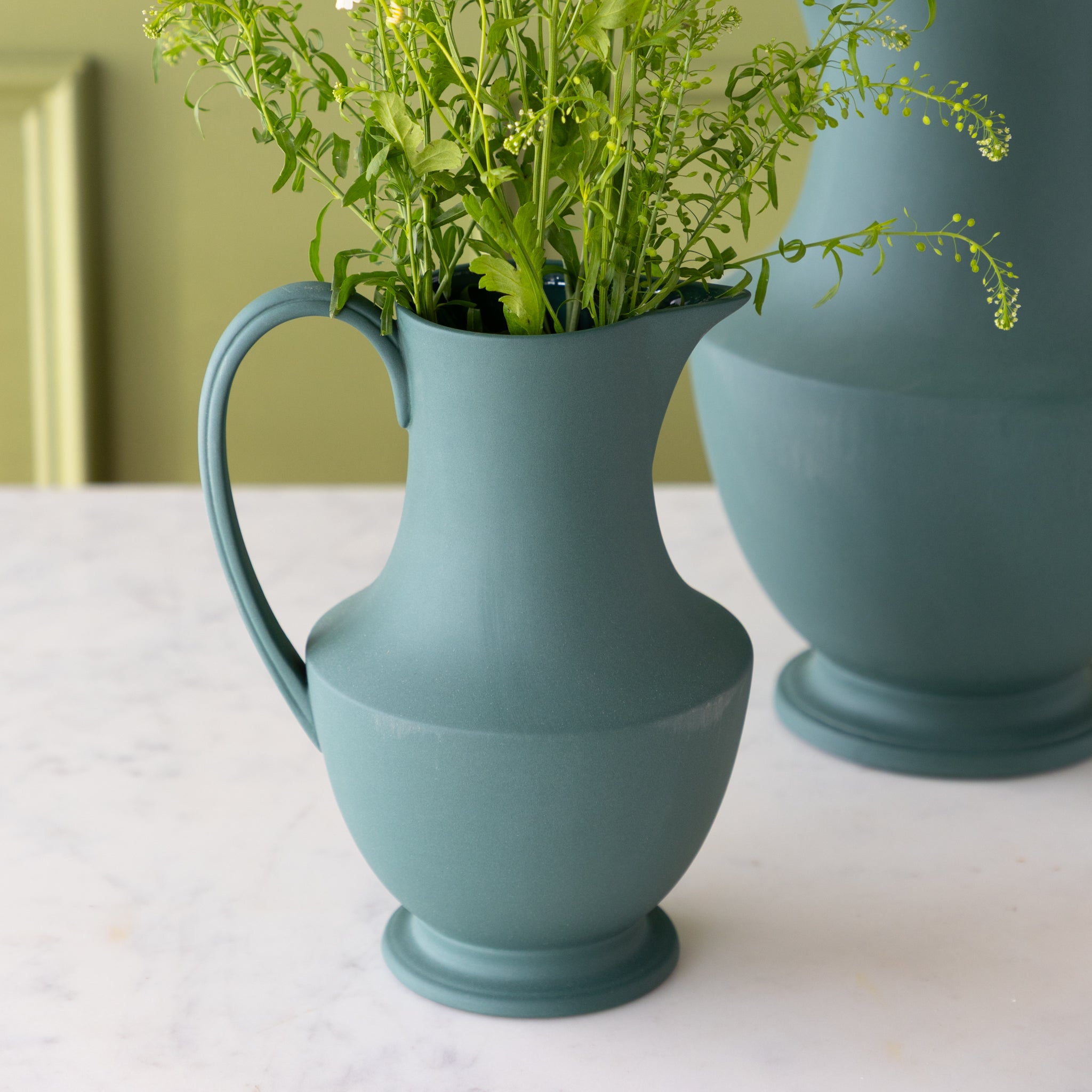 Toulouse Verdant Green Pitcher with flowers in it on a marble table.