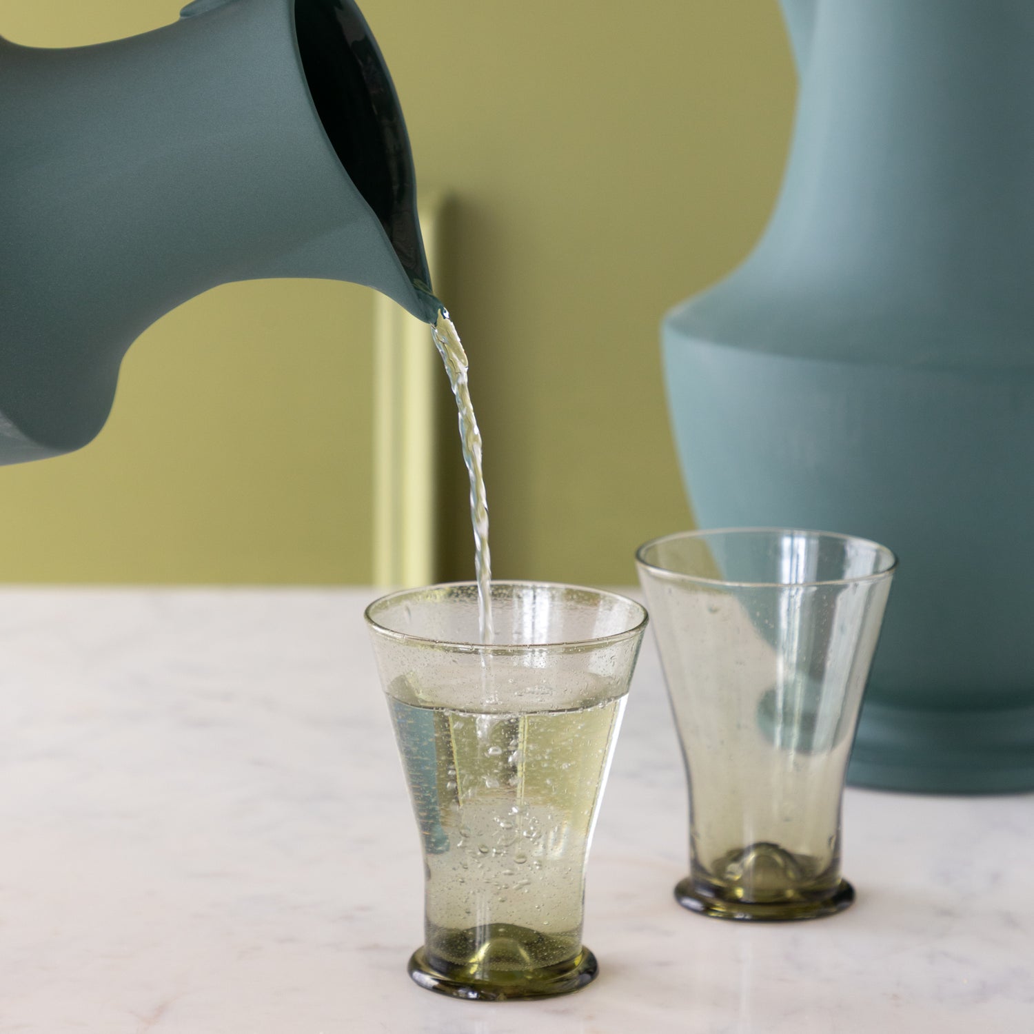 Toulouse Verdant Green Pitcher pouring water into a glass on a marble table.