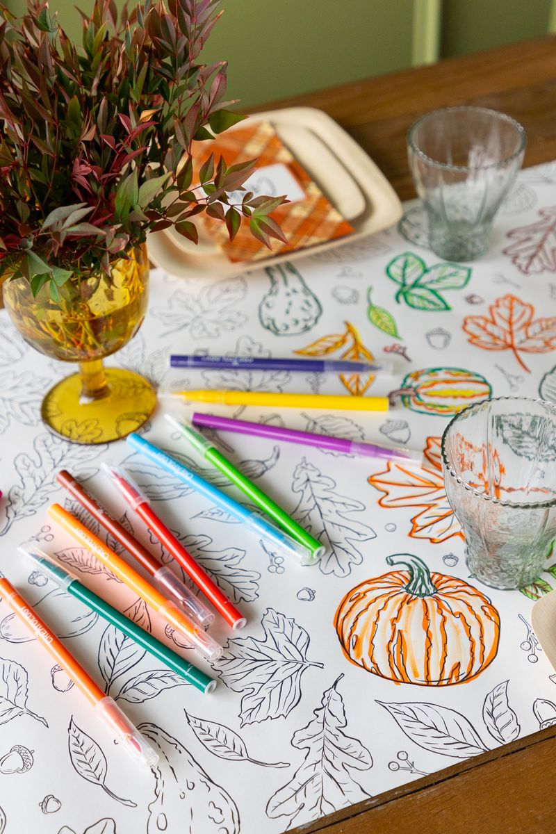 A fall tablescape featuring a partially colored in Autumn Coloring Runner, with colorful markers scattered on the table.