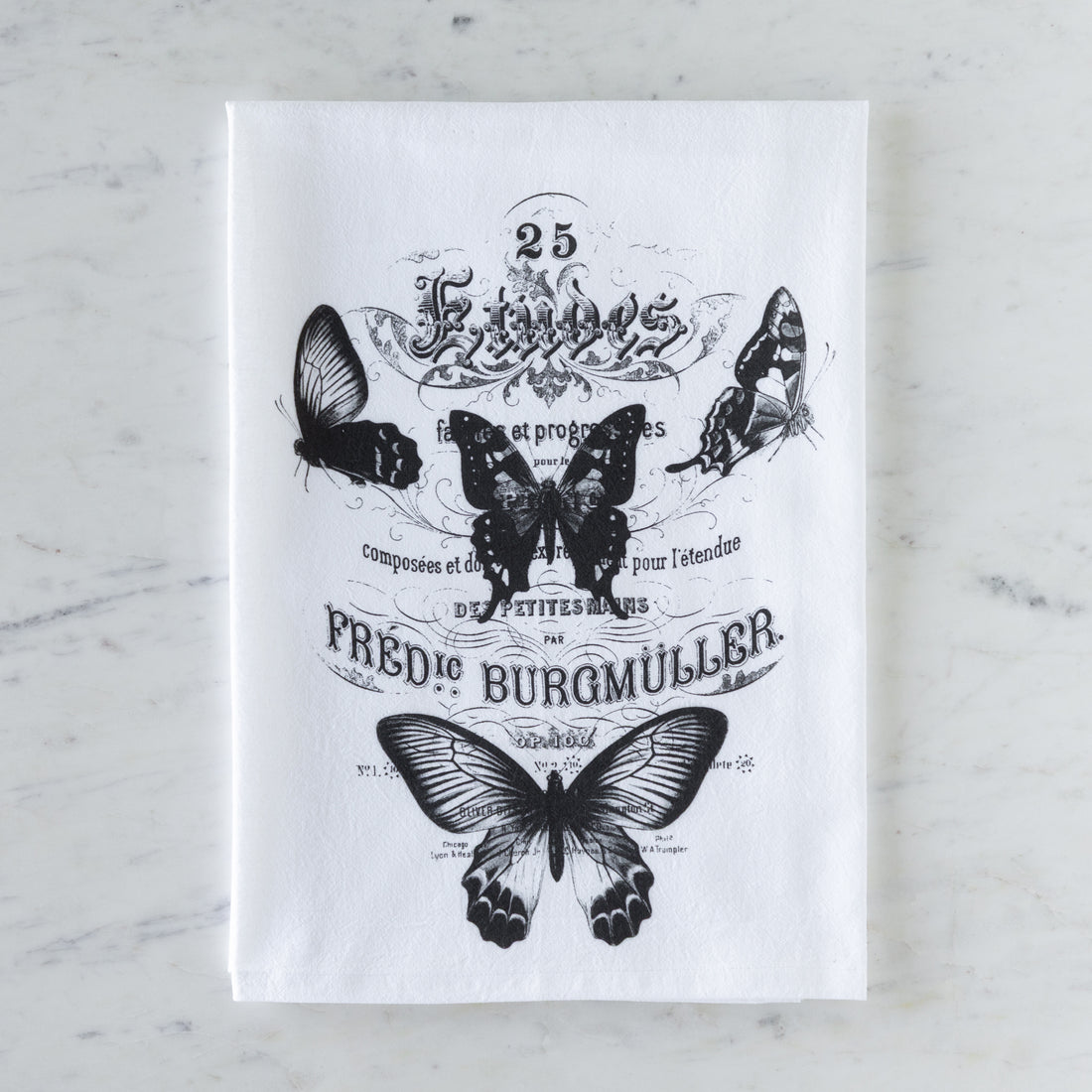 White tea towel with black butterfly illustrations and text on a marble surface.