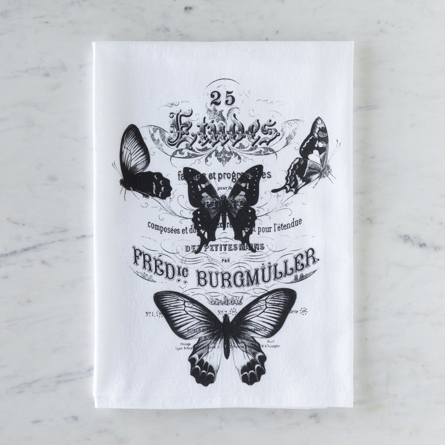 White tea towel with black butterfly illustrations and text on a marble surface.