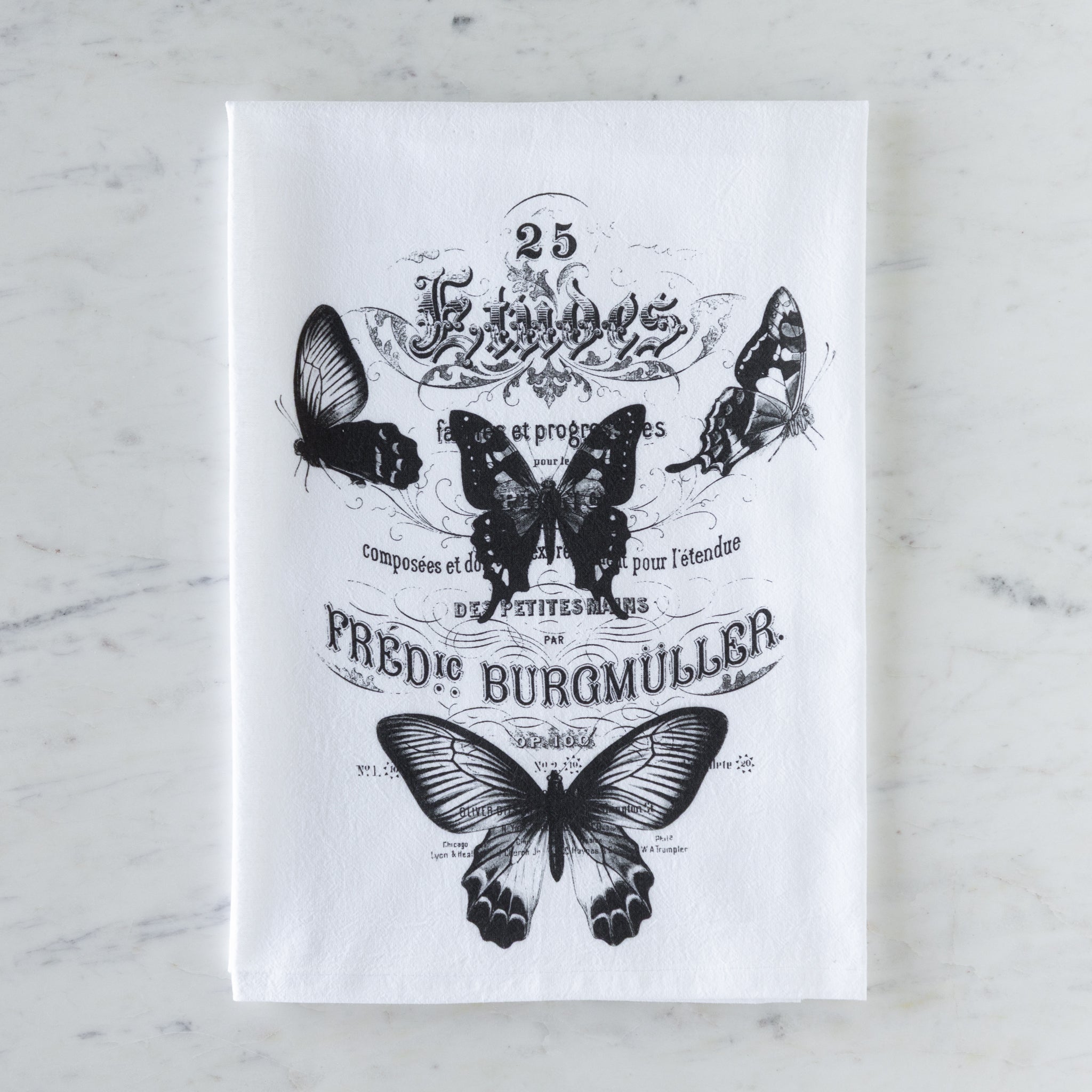 White tea towel with black butterfly illustrations and text on a marble surface.