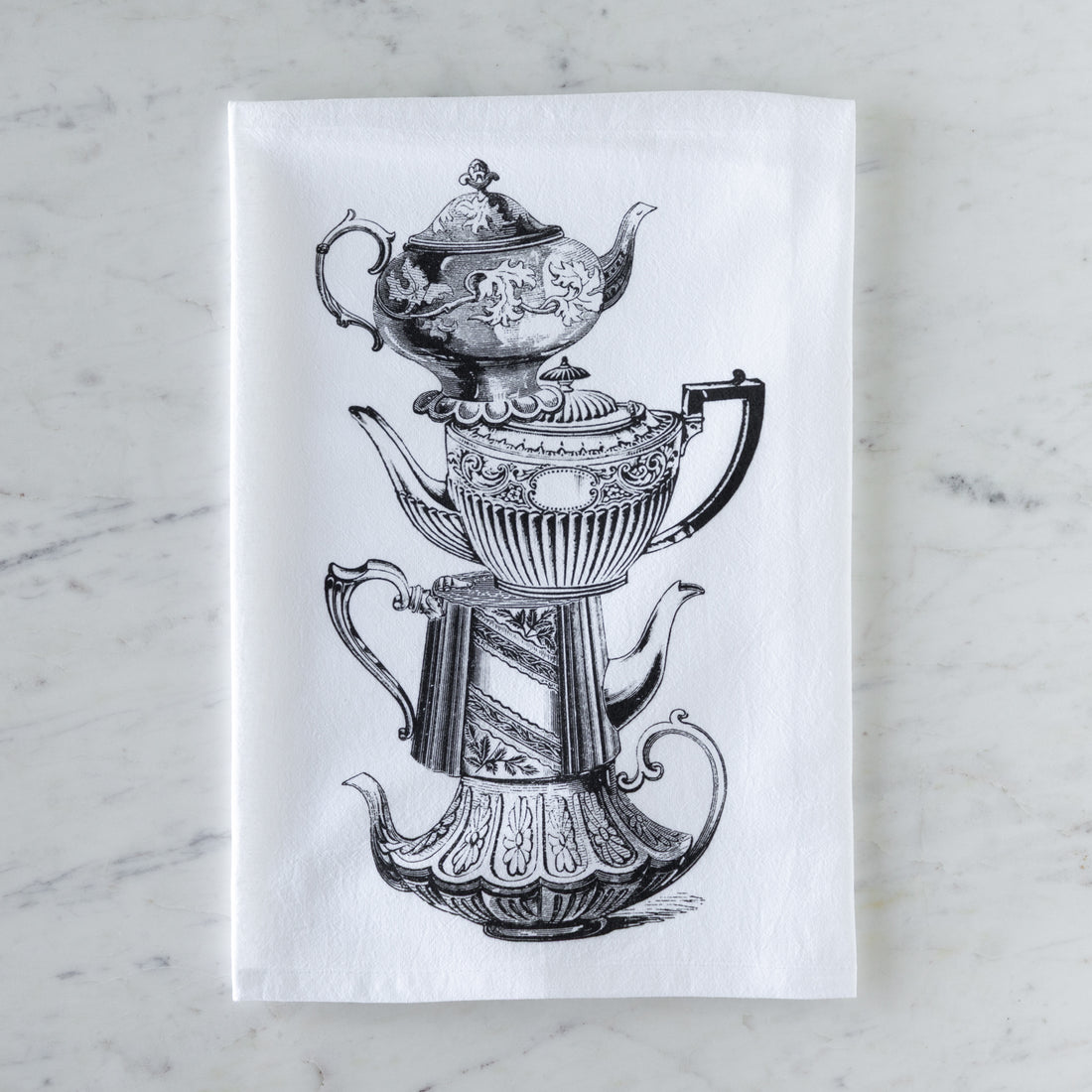Tea towel with black and white illustration of vintage stacked teapots on a marble surface.