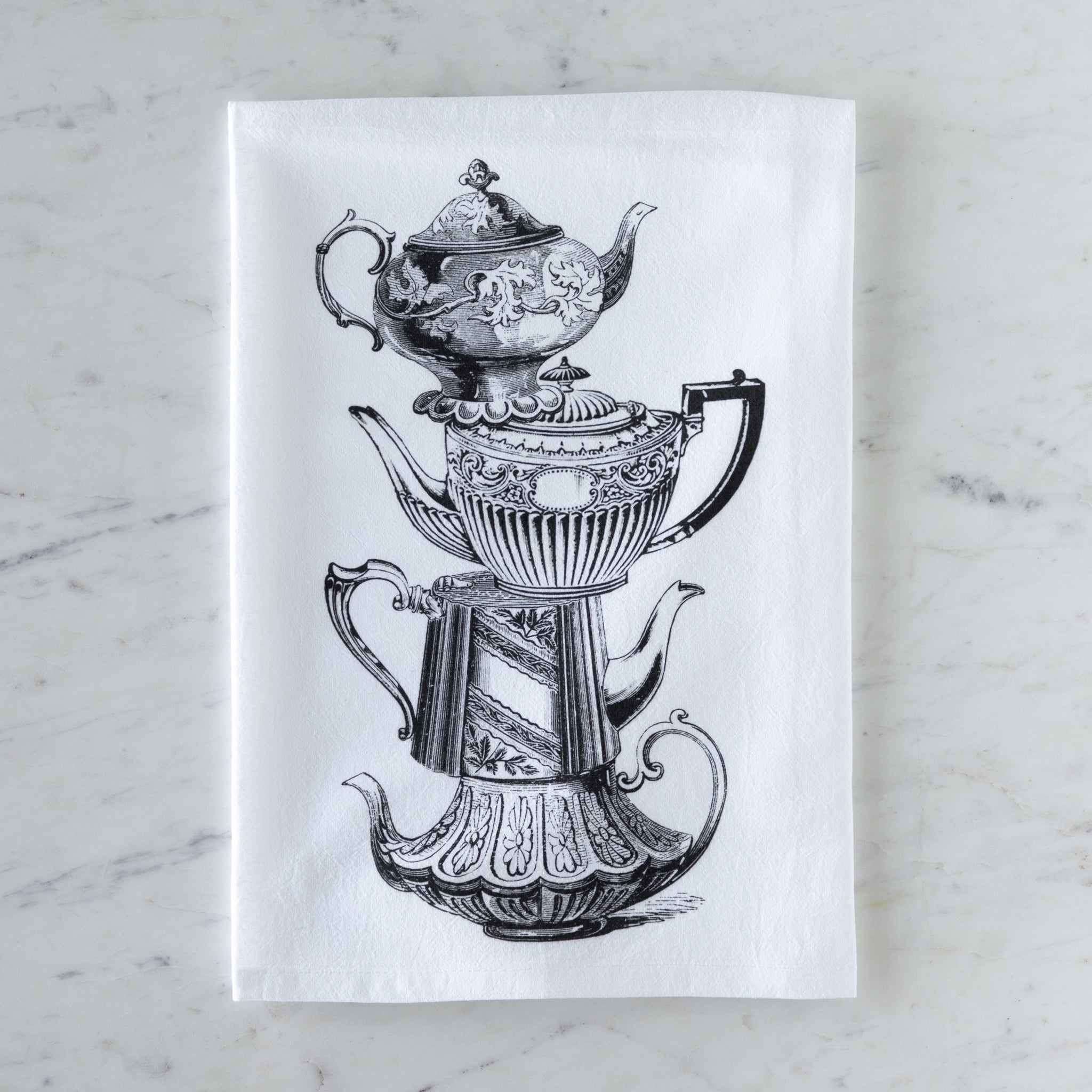 Tea towel with black and white illustration of vintage stacked teapots on a marble surface.
