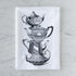 Tea towel with black and white illustration of vintage stacked teapots on a marble surface.