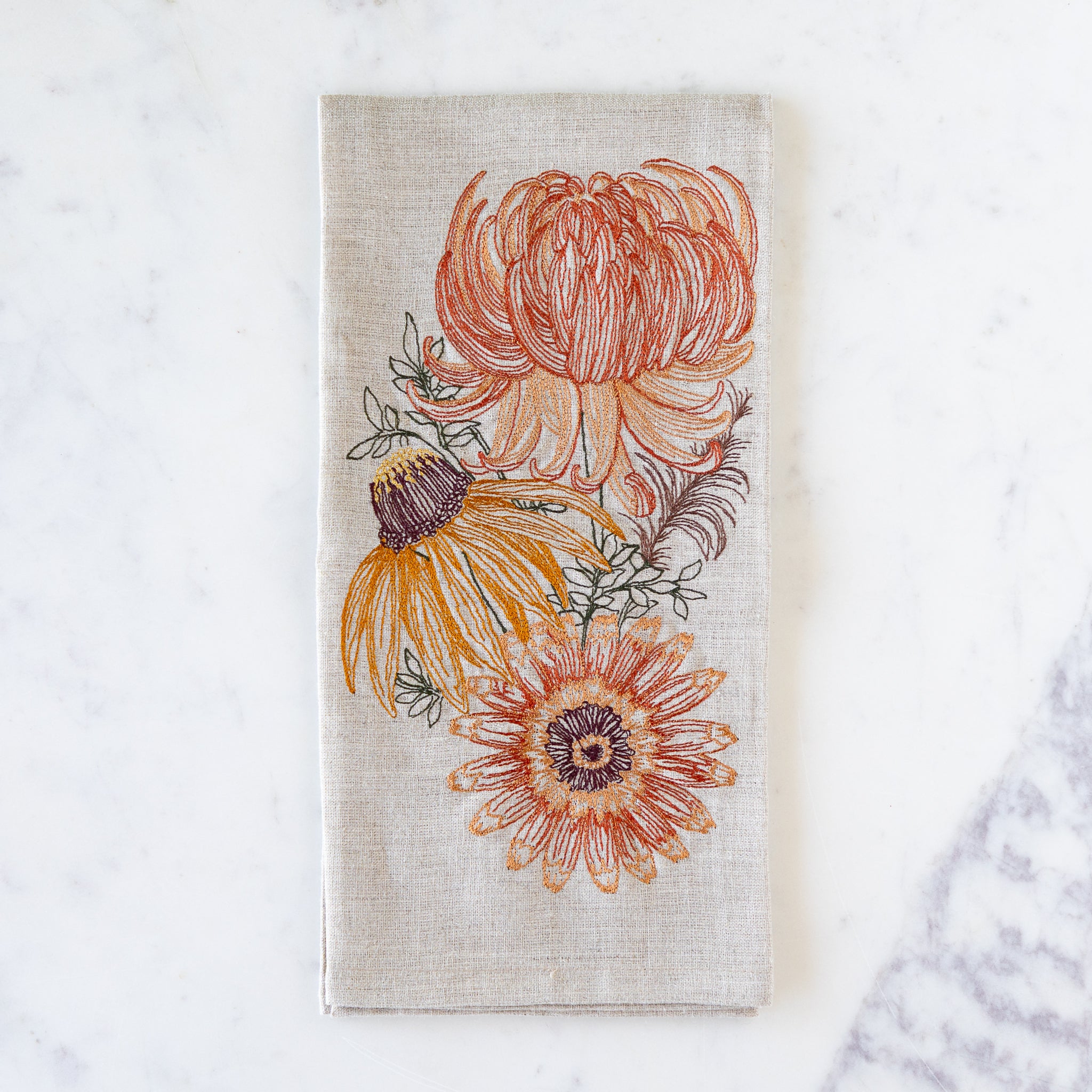 Floral design of autumn mums, a sunflower and leaves on a towel against a white background.
