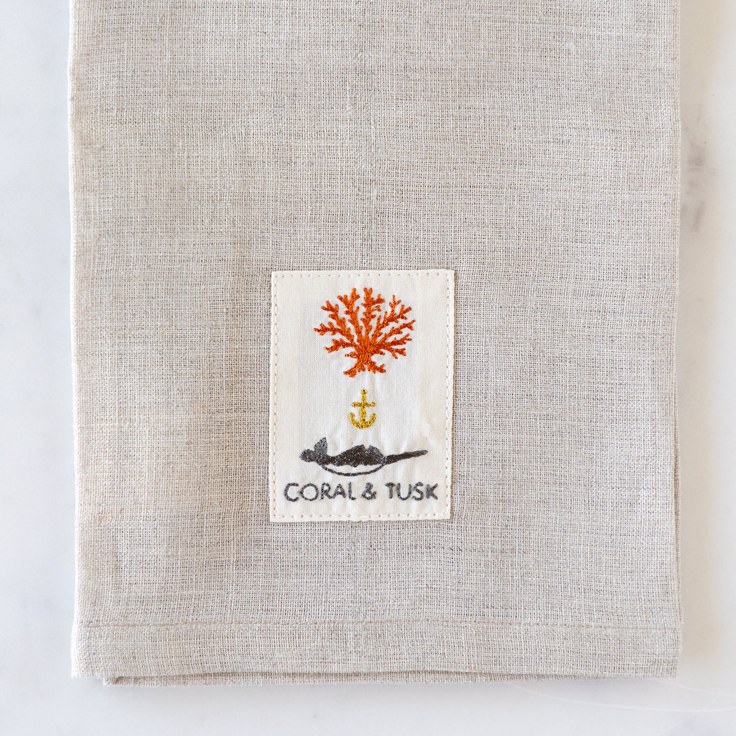 Textile product with a label featuring coral and an anchor design on a neutral background.