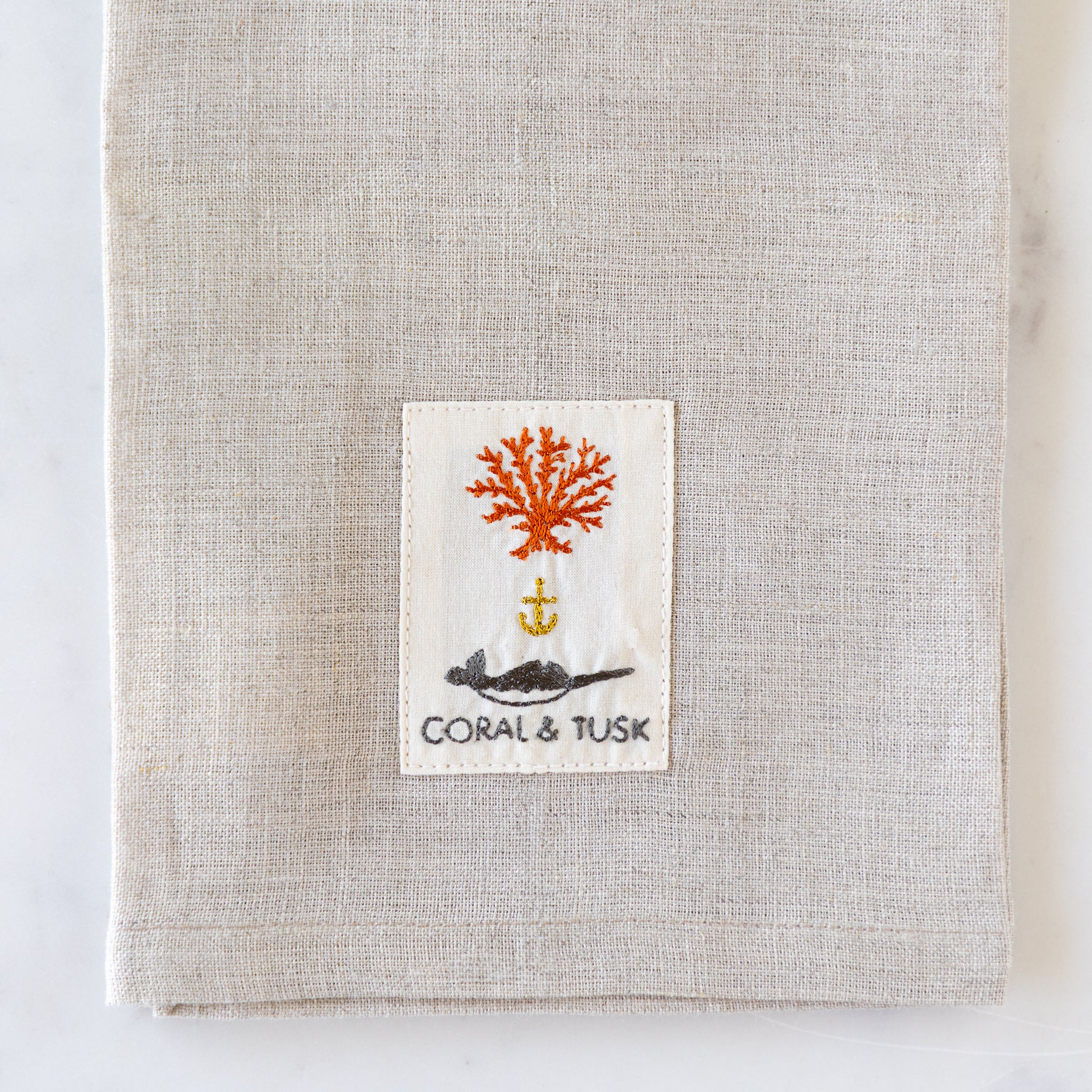 Textile product with a label featuring coral and an anchor design on a neutral background.