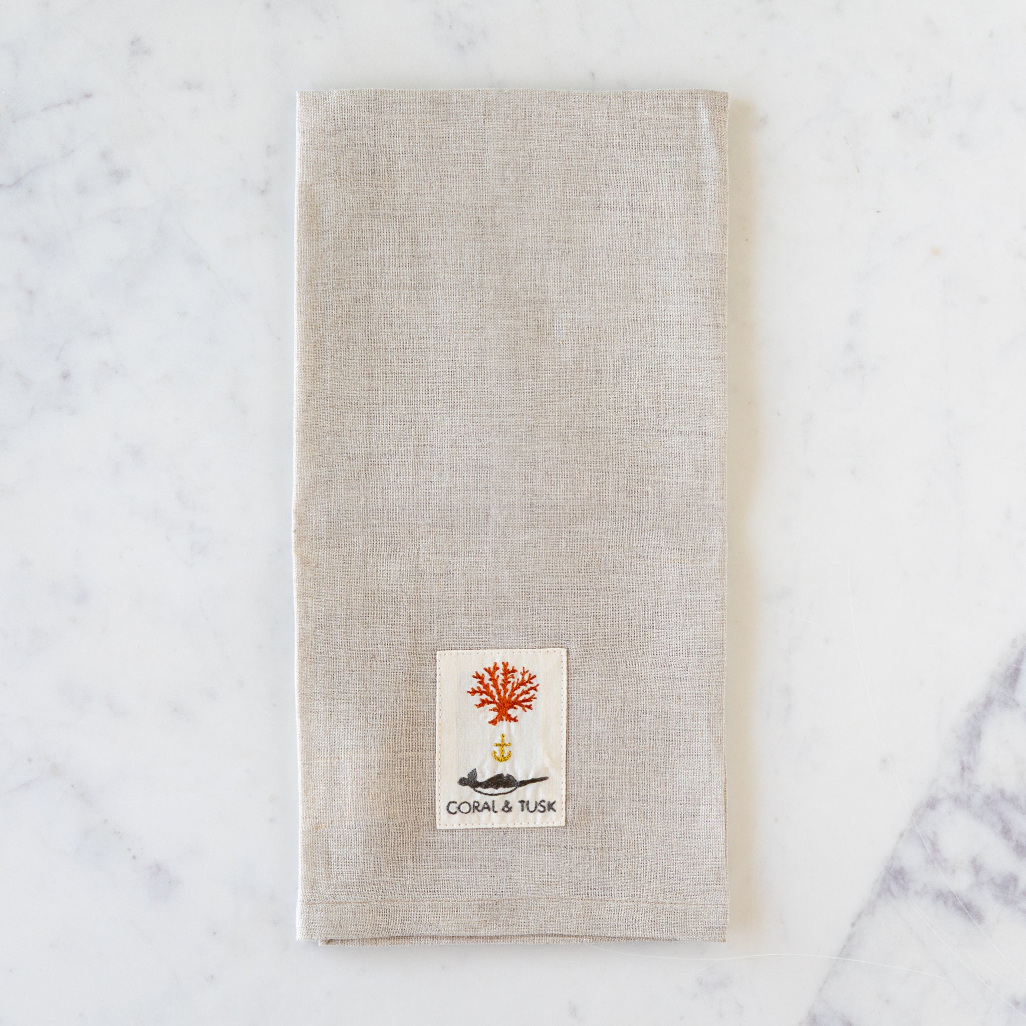 Beige towel with a Coral &amp; Tusk logo on a marble surface.