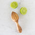 Olive wood Citrus Juicer on a marble table with two lime halves.
