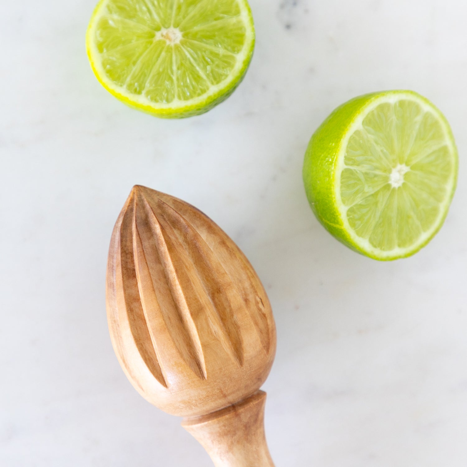 Wooden citrus juicer with two halves of a lime on a white surface.
