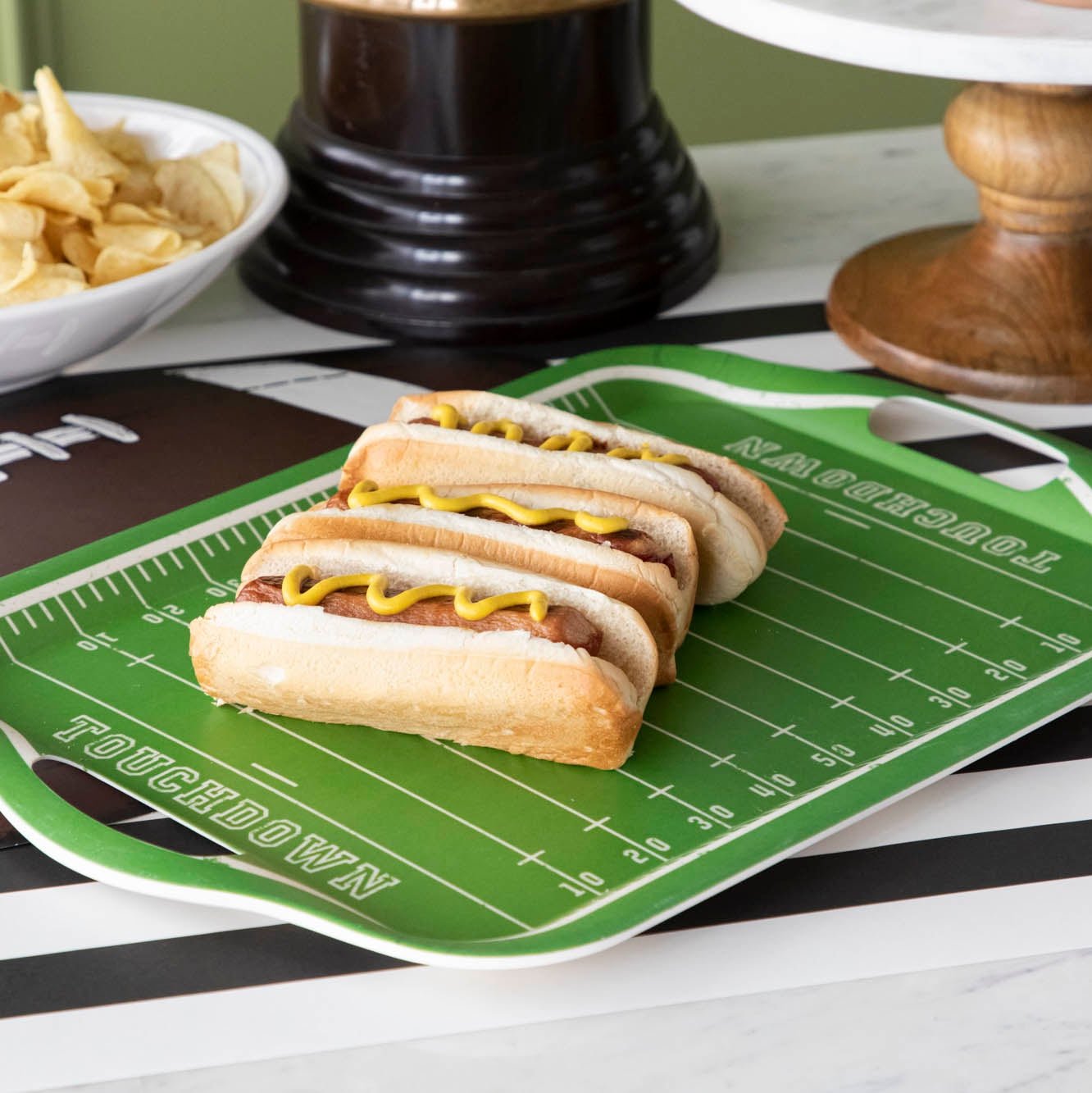 A football field tray with hot dogs on top on a football themed table setting. 