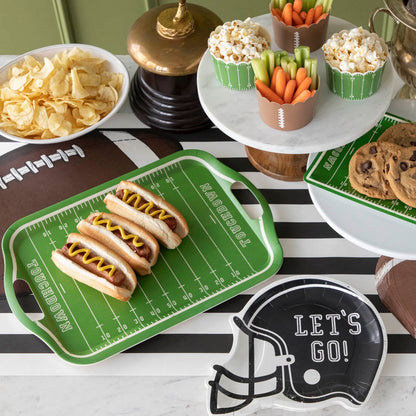 A football themed table setting with various snacks and a football field tray with hot dogs.