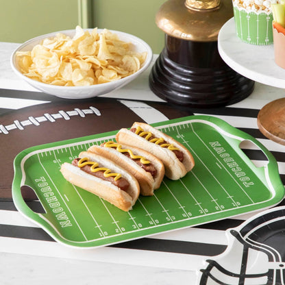 A football field tray with hot dogs on top on a football themed table setting. 