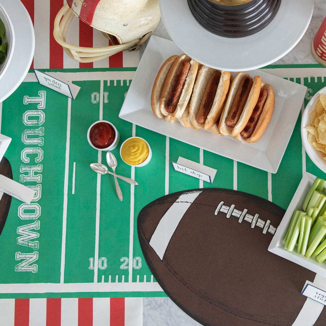 Football themed table setting featuring a Touchdown Football Field Runner with a Die-cut Football Placemat on top and various game day snacks.