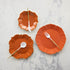 A set of orange scalloped plates with gold rims on a white background, accompanied by white utensils with gold accents.