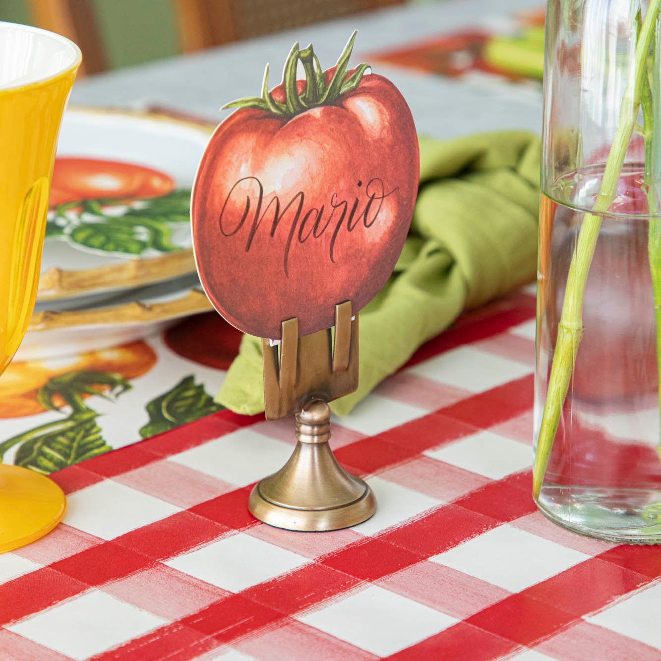 Tomato Place Card with &quot;Mario&quot; written on it, held by the Brass Place Card Holder, behind a place setting.