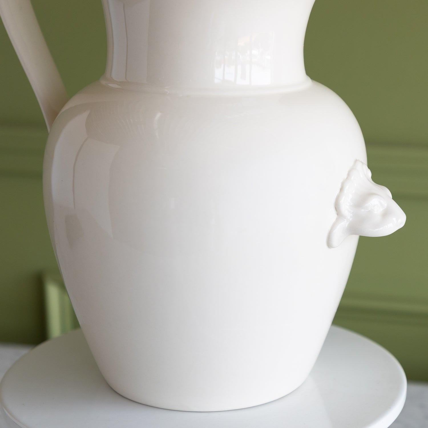 White ceramic pitcher with a lion finial on a green background.