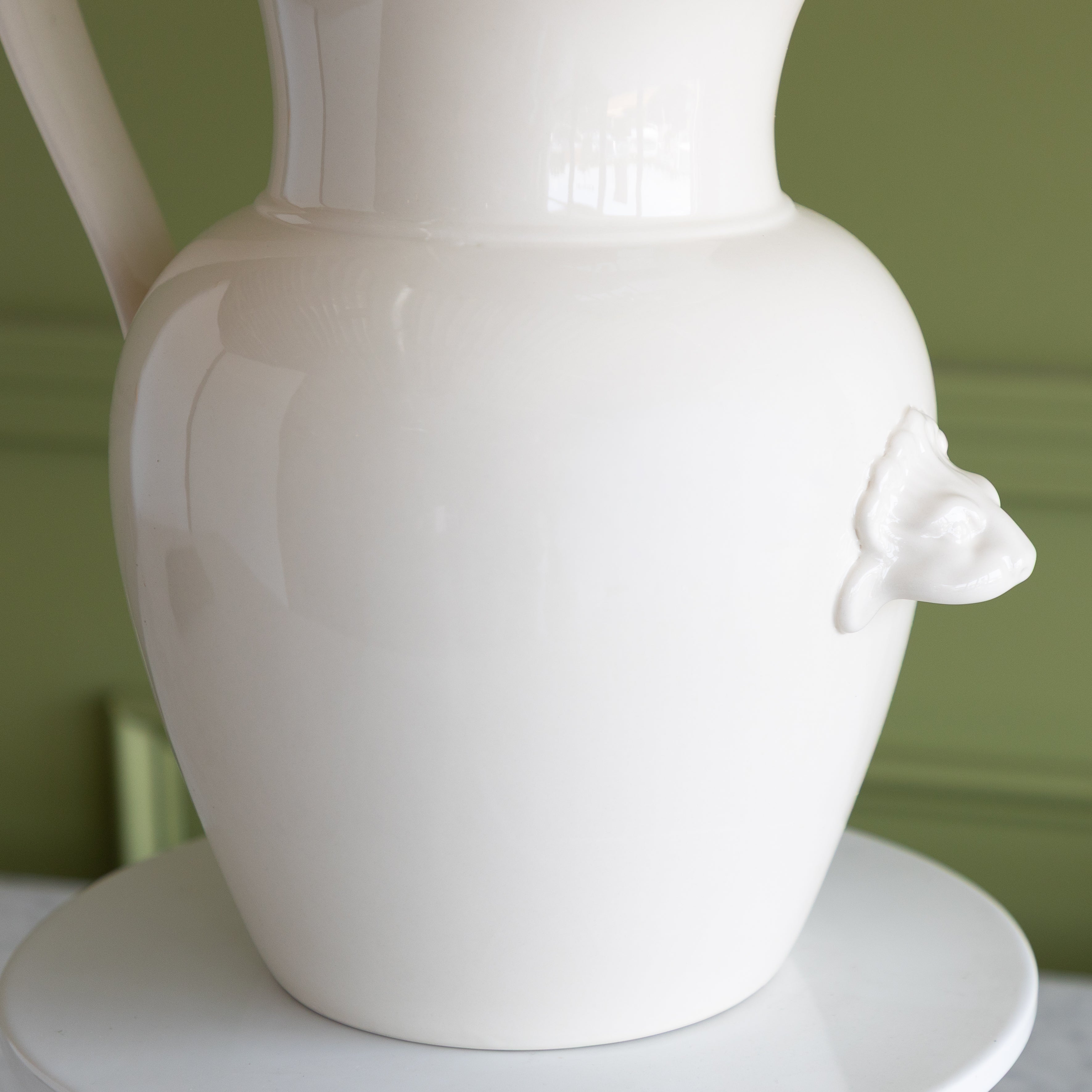 White ceramic pitcher with a lion finial on a green background.