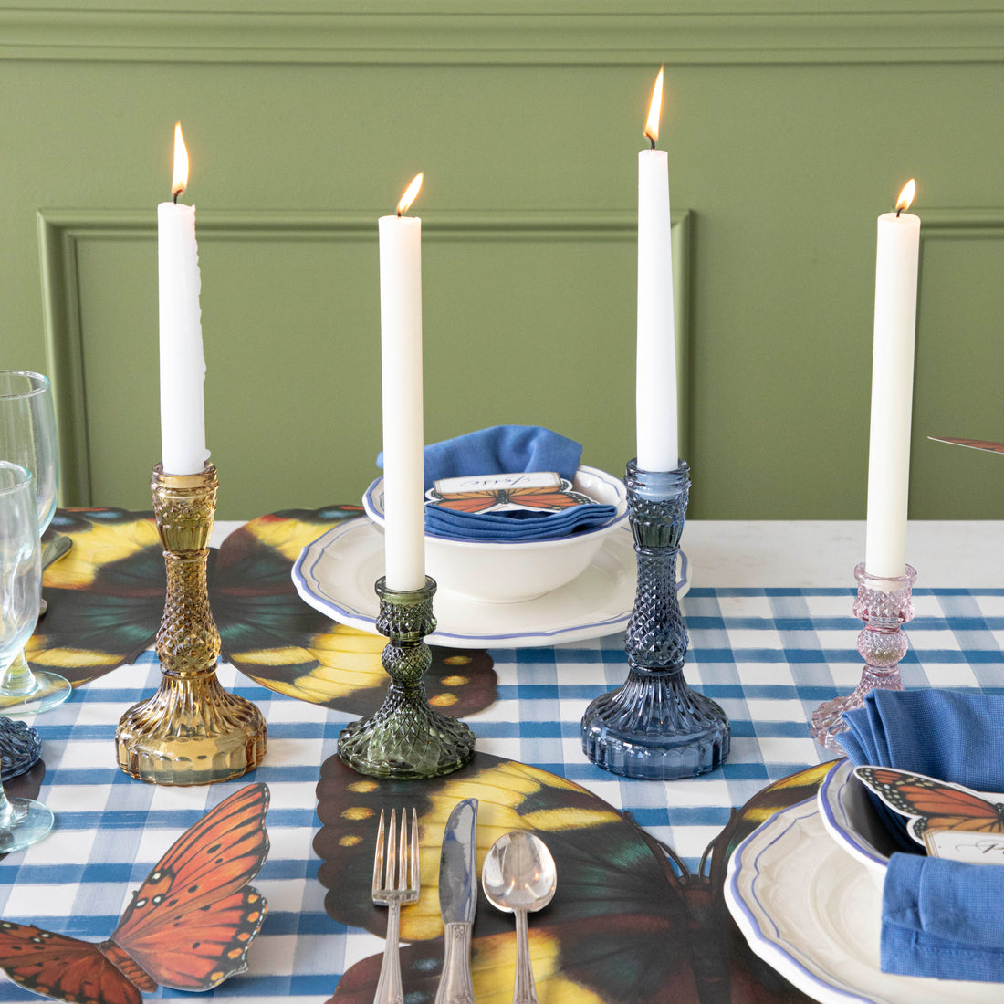 A yellow, green, blue and pink candle holder each with a let white candle all on a set table. 