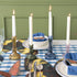 A yellow, green, blue and pink candle holder each with a let white candle all on a set table. 