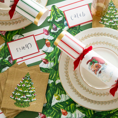 An elegant table setting with a stack of the Vintage Christmas Tree Cocktail Napkins next to two dinner plates with a Santa Cracker on top.