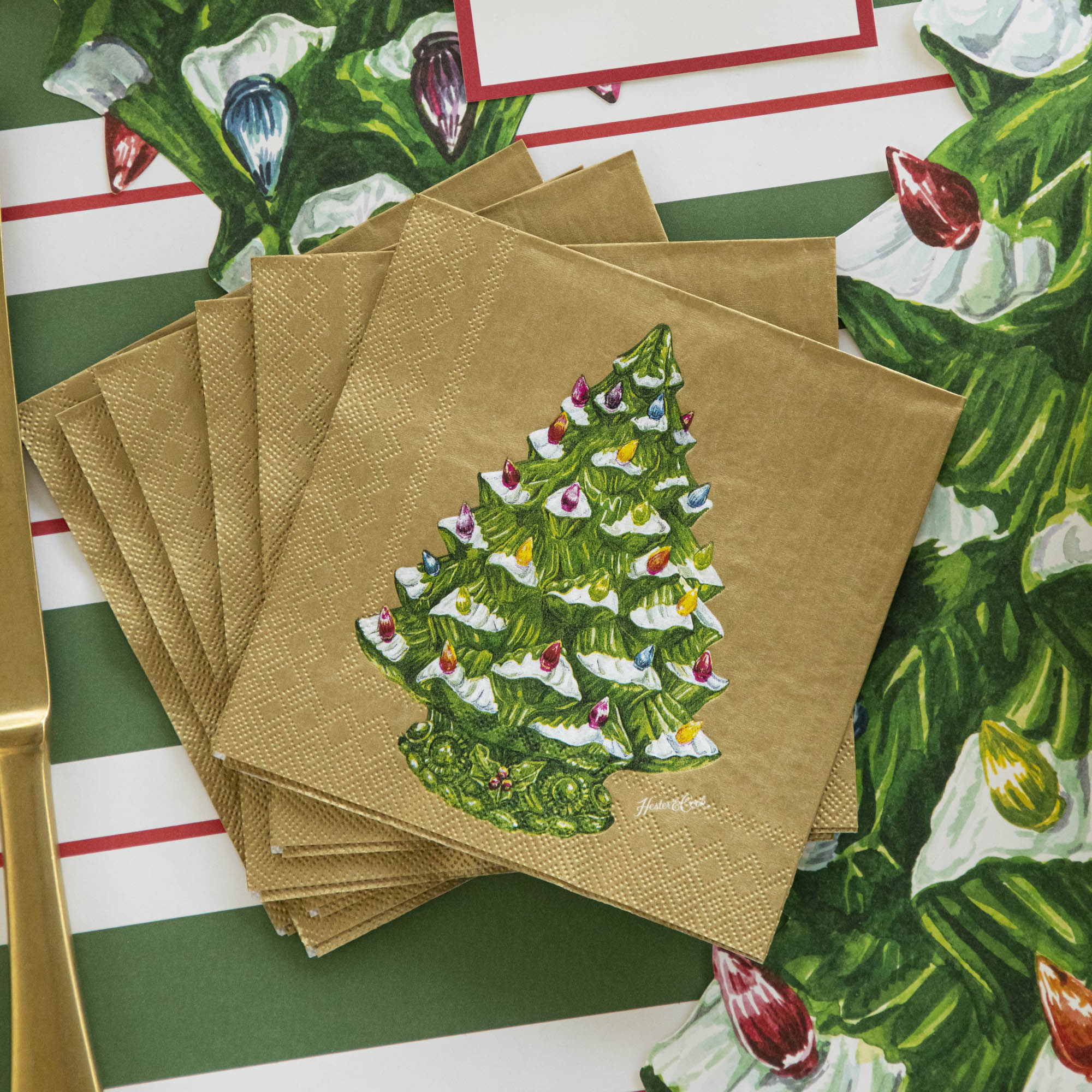 A fanned out stack of the Vintage Christmas Tree Cocktail Napkins on the Green &amp; Red Awning Stripe Runner and Vintage Christmas Tree Placemat.