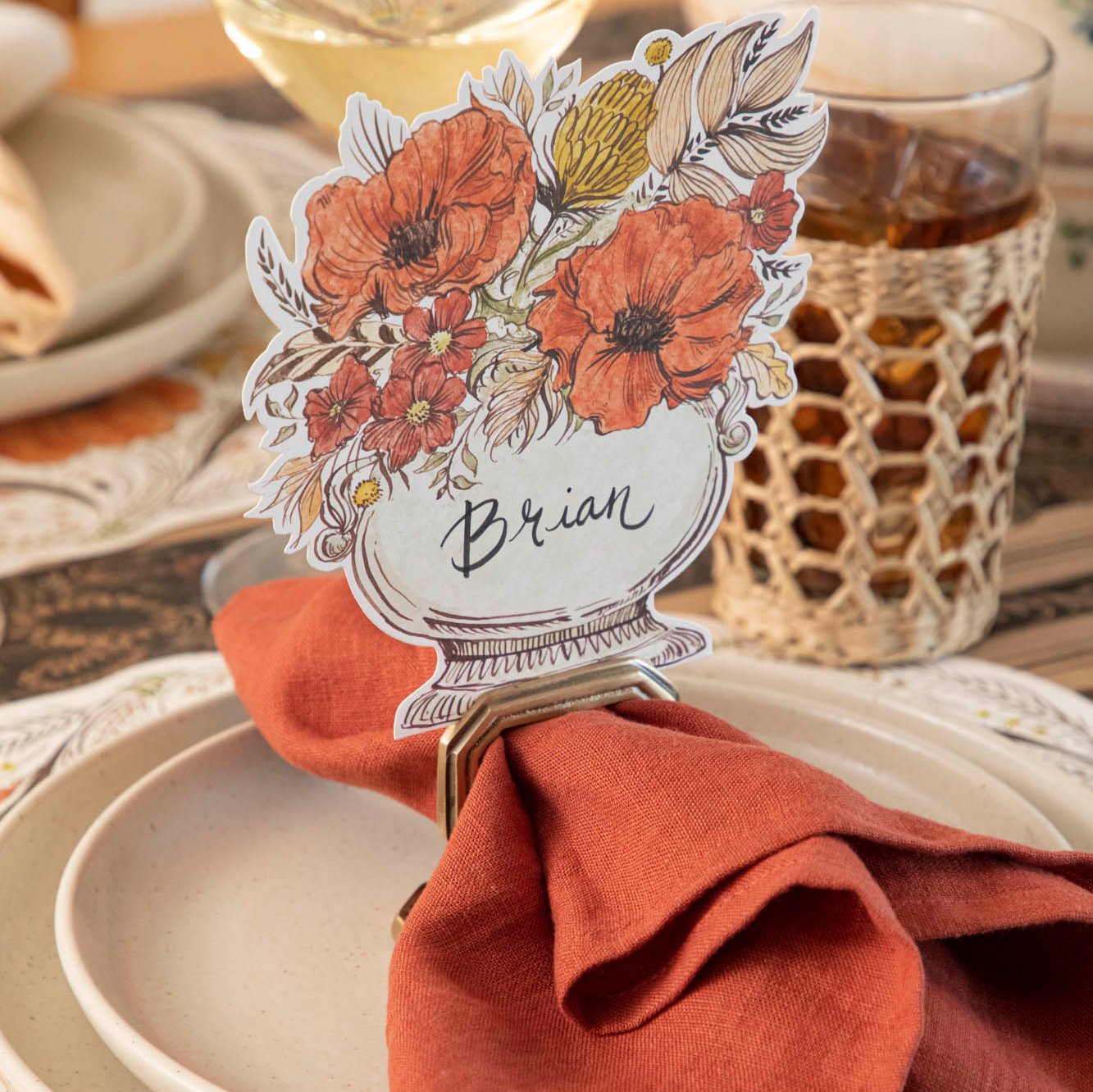 A close up view of the Autumn Arrangement Place Card with the name "Brian" written on it, on a fall themed table setting.