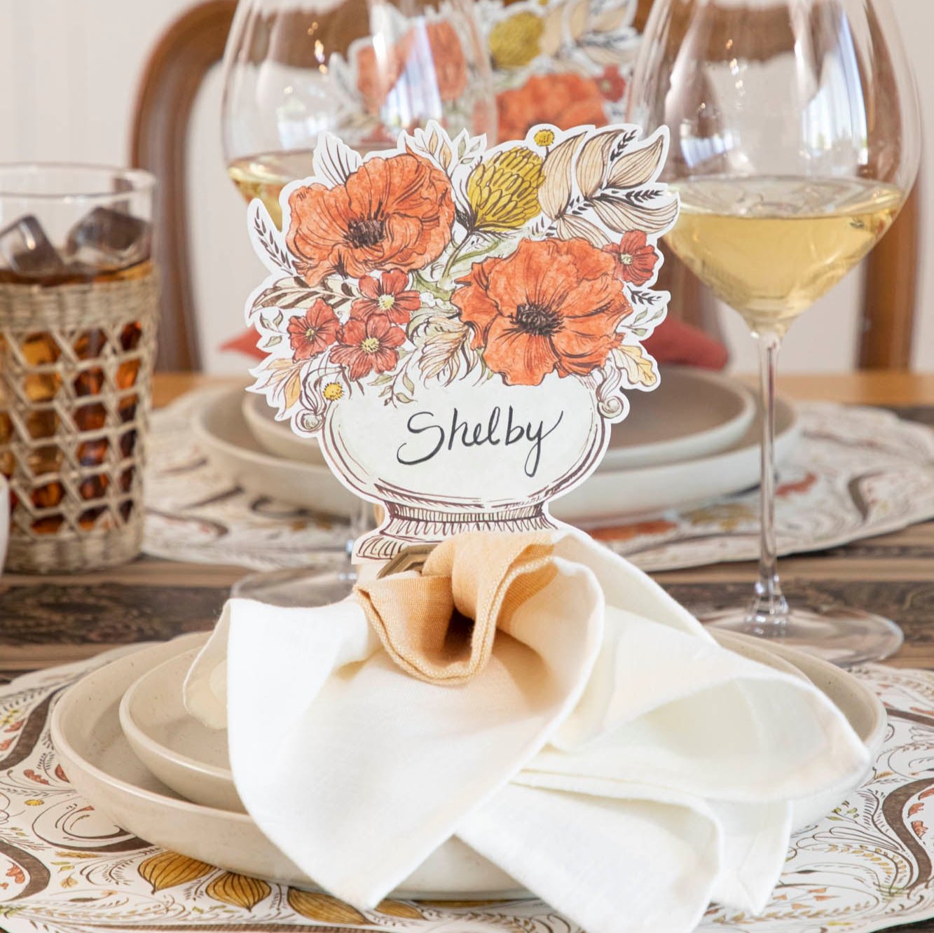 The Autumn Arrangement Place Card with the name "Shelby" written on it, on an elegant fall themed table setting.