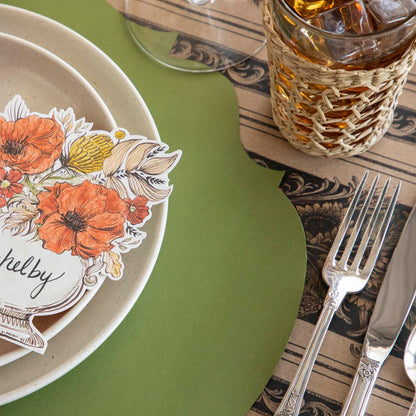 An elegant table setting with a Green French Frame placemat on a Vintage Sunflower stripe runner with cream dinner plates, a napkin and Autumn Arrangement Place card on the plates.