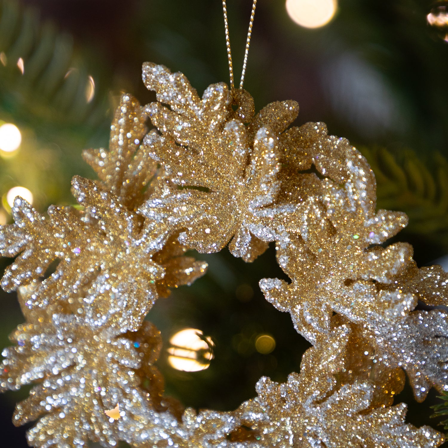 Decorative gold wreath ornament on a Christmas tree with blurred lights in the background.