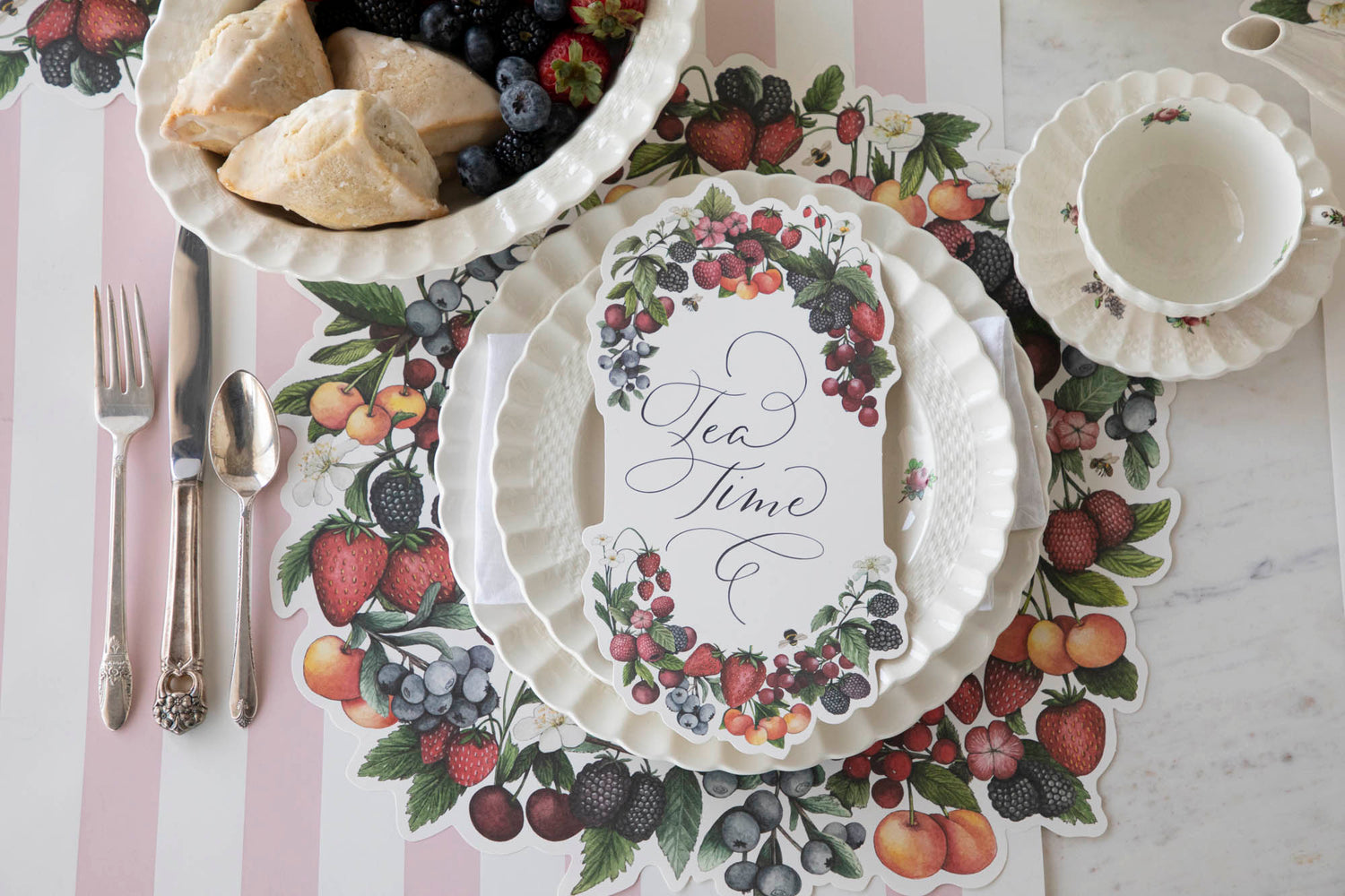 A Die-cut Berry Wreath Placemat by Hester &amp; Cook with a plate and bowl of fruit on a table.