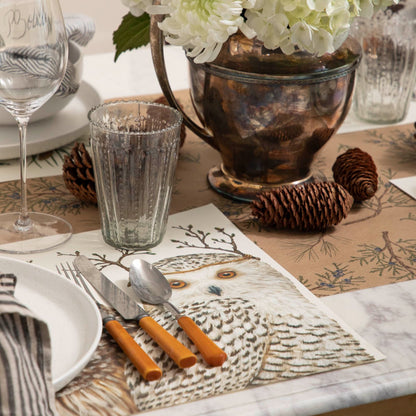 Winter Owls Placemat with brown handled silverware and glasses on top of a Juniper Sprigs runner and pinecones nearby.