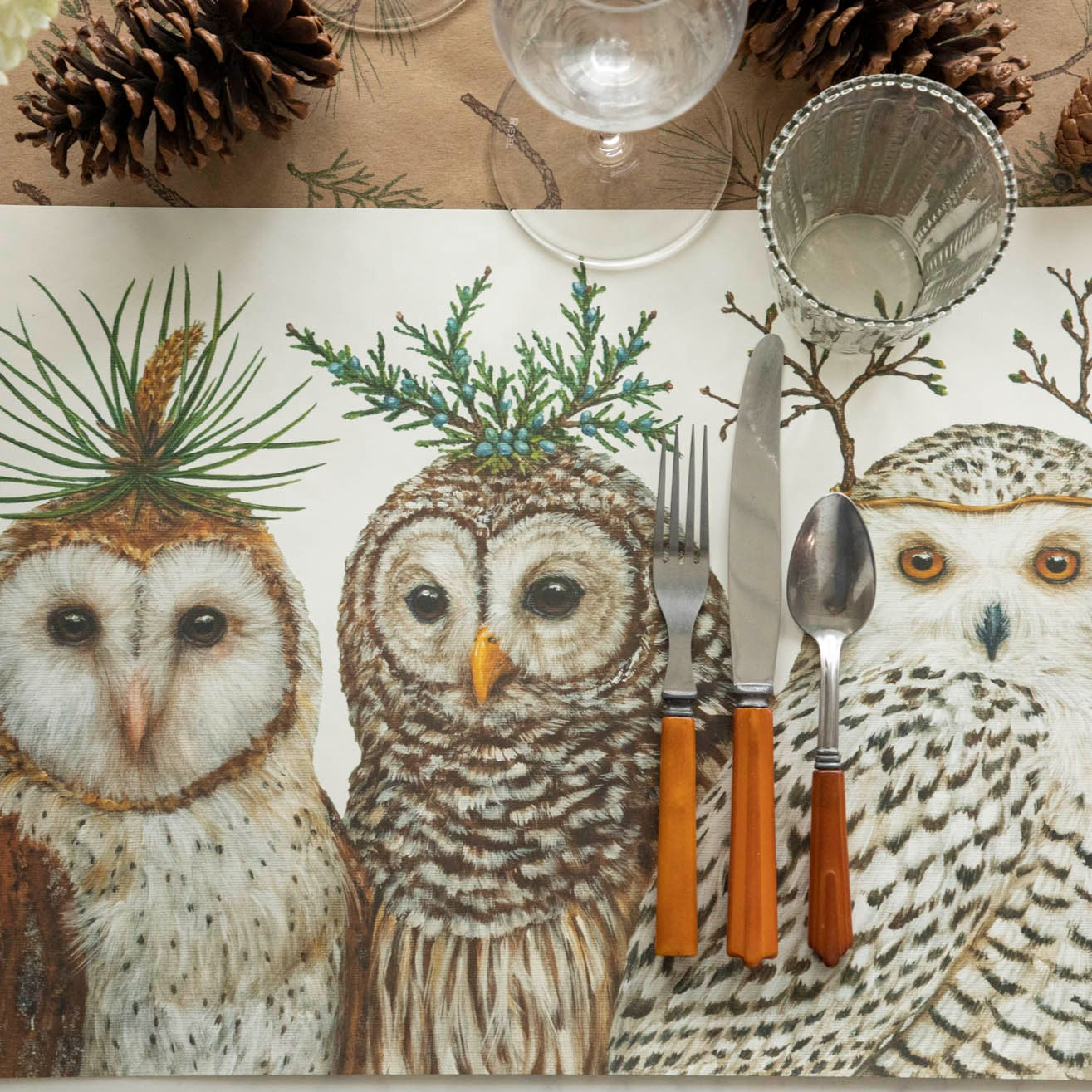 Winter Owls Placemat with brown handled silverware and glasses on top of a Juniper Sprigs runner and pinecones nearby.