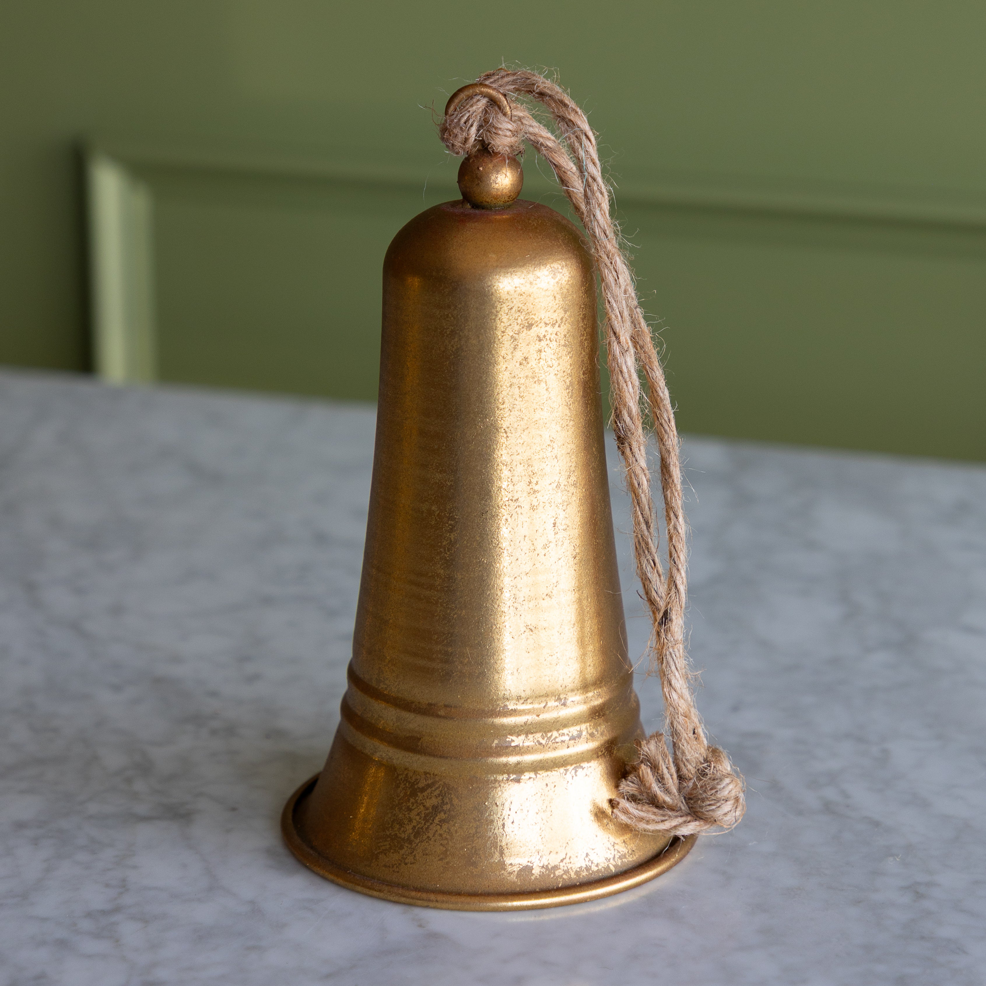 Gold bell with a rope on a marble surface with a green wall background