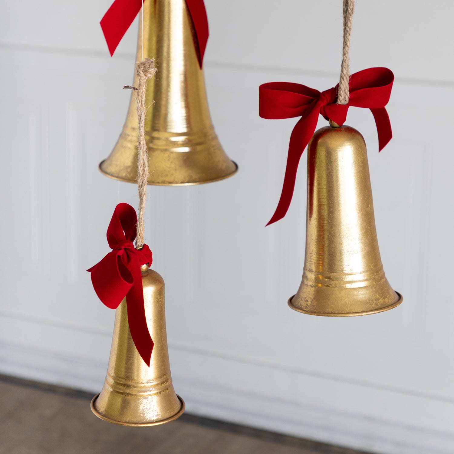 Three gold bells with red ribbons hanging against a white background