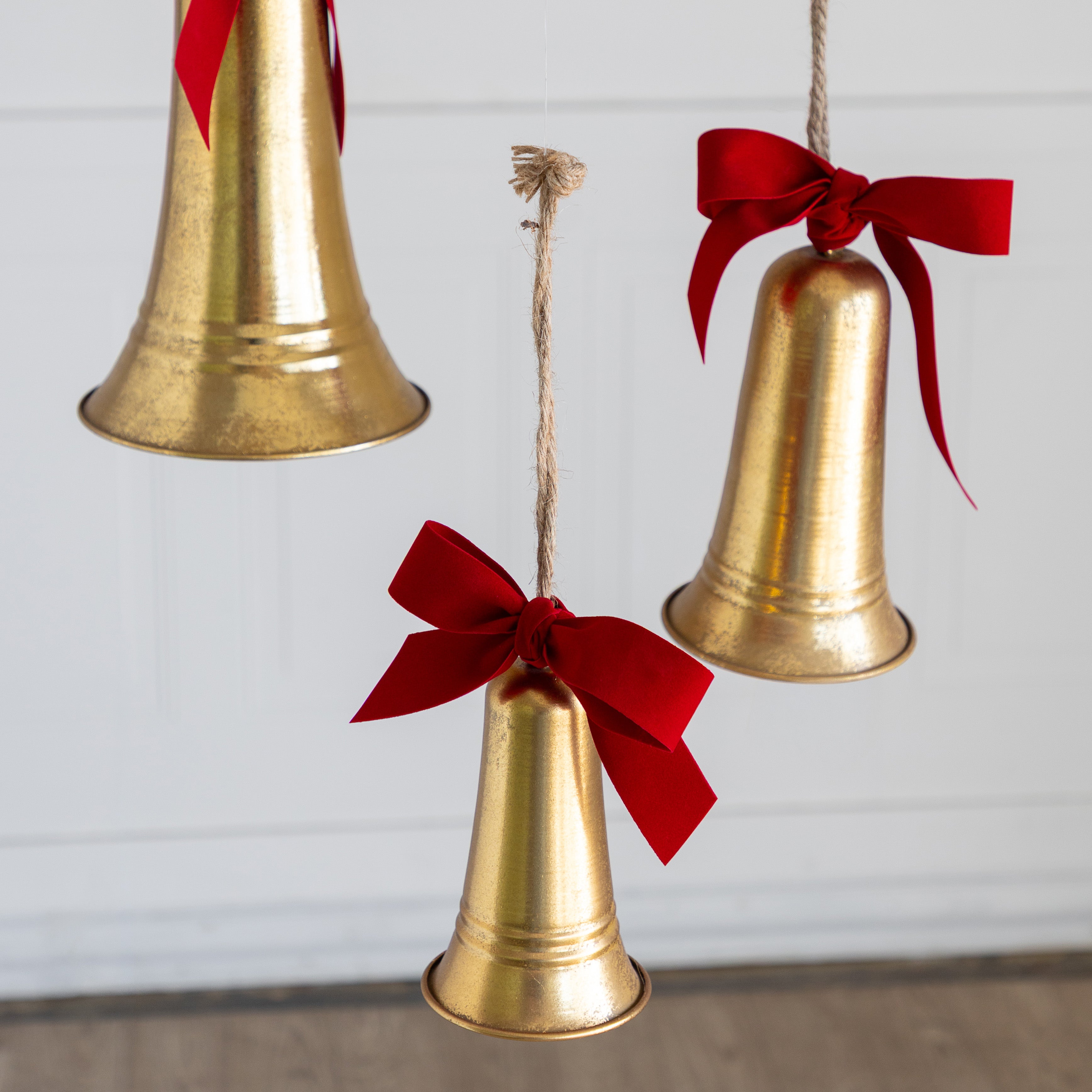 Three gold bells with red ribbons hanging against a light background