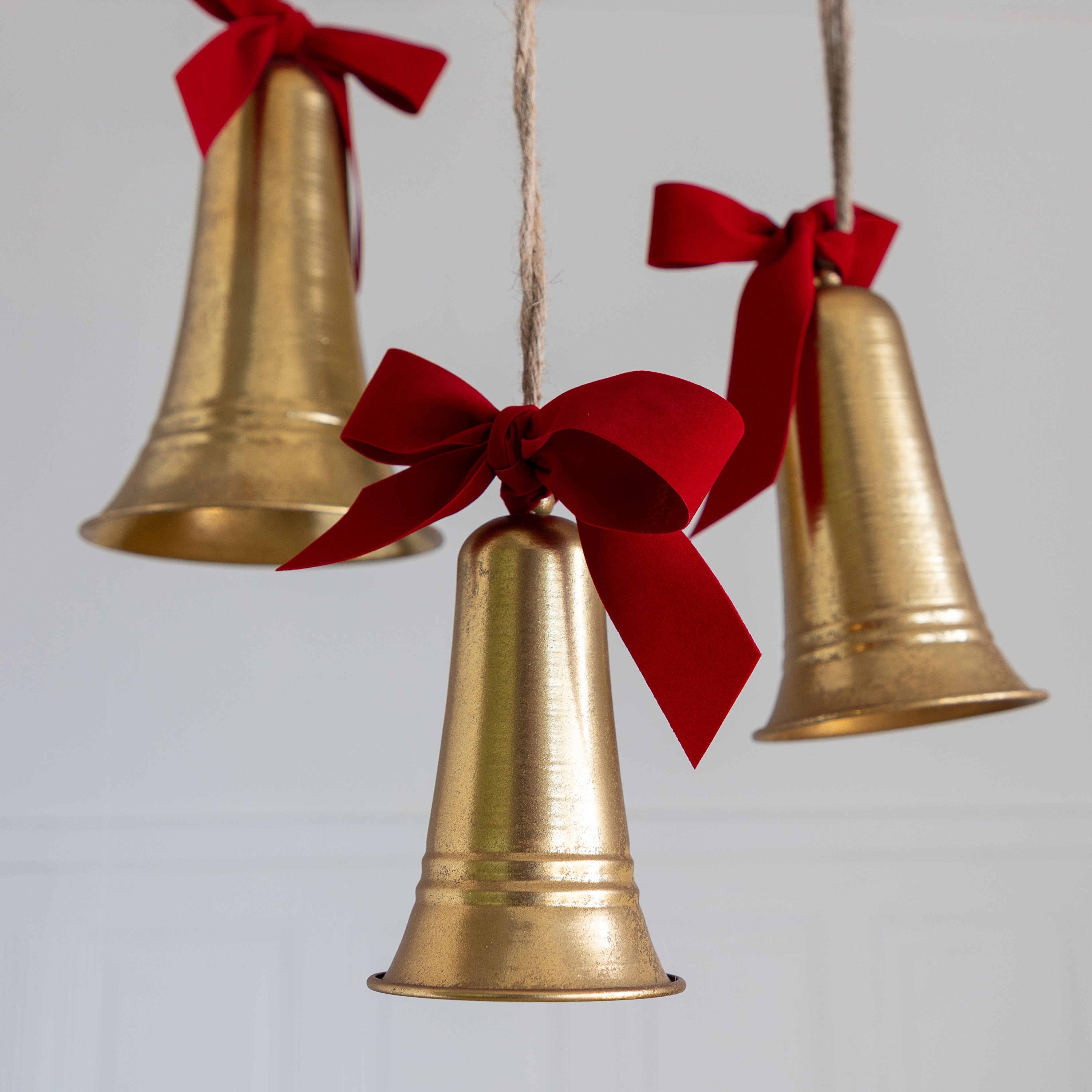 Three gold bells with red ribbons hanging against a light gray background