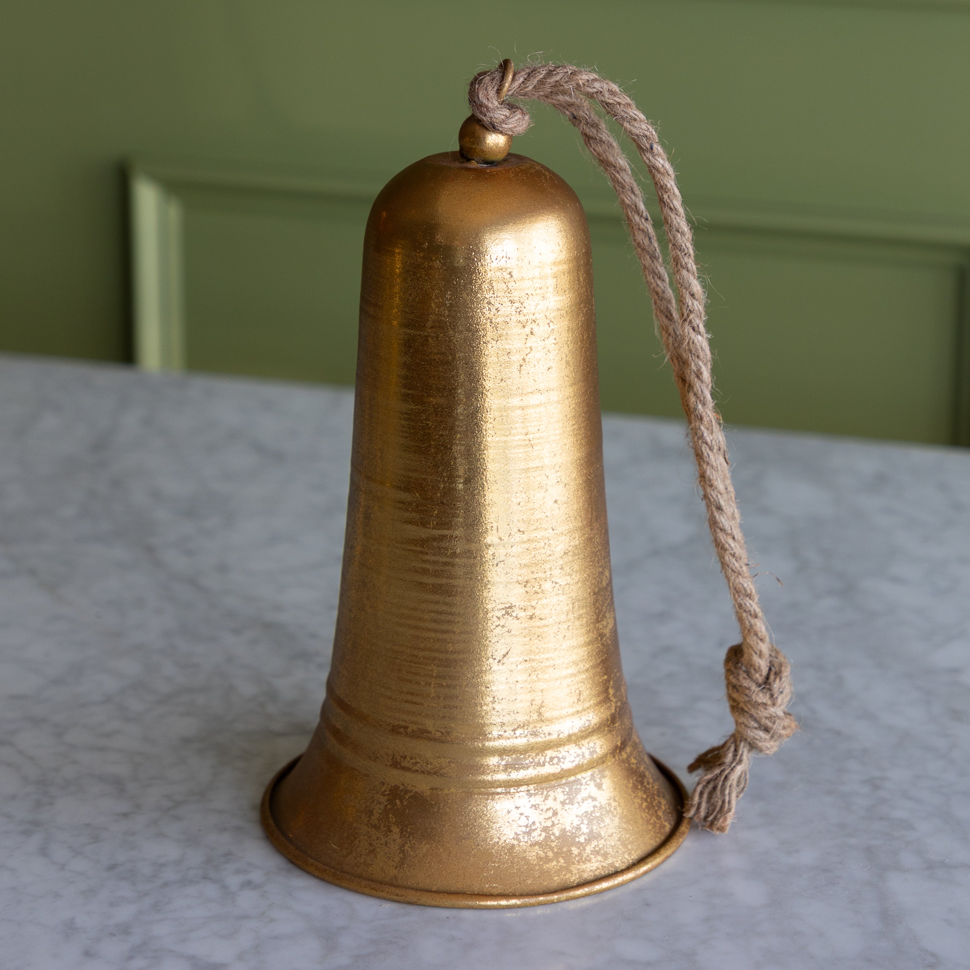 Bronze bell with a rope on a textured surface with a green wall background