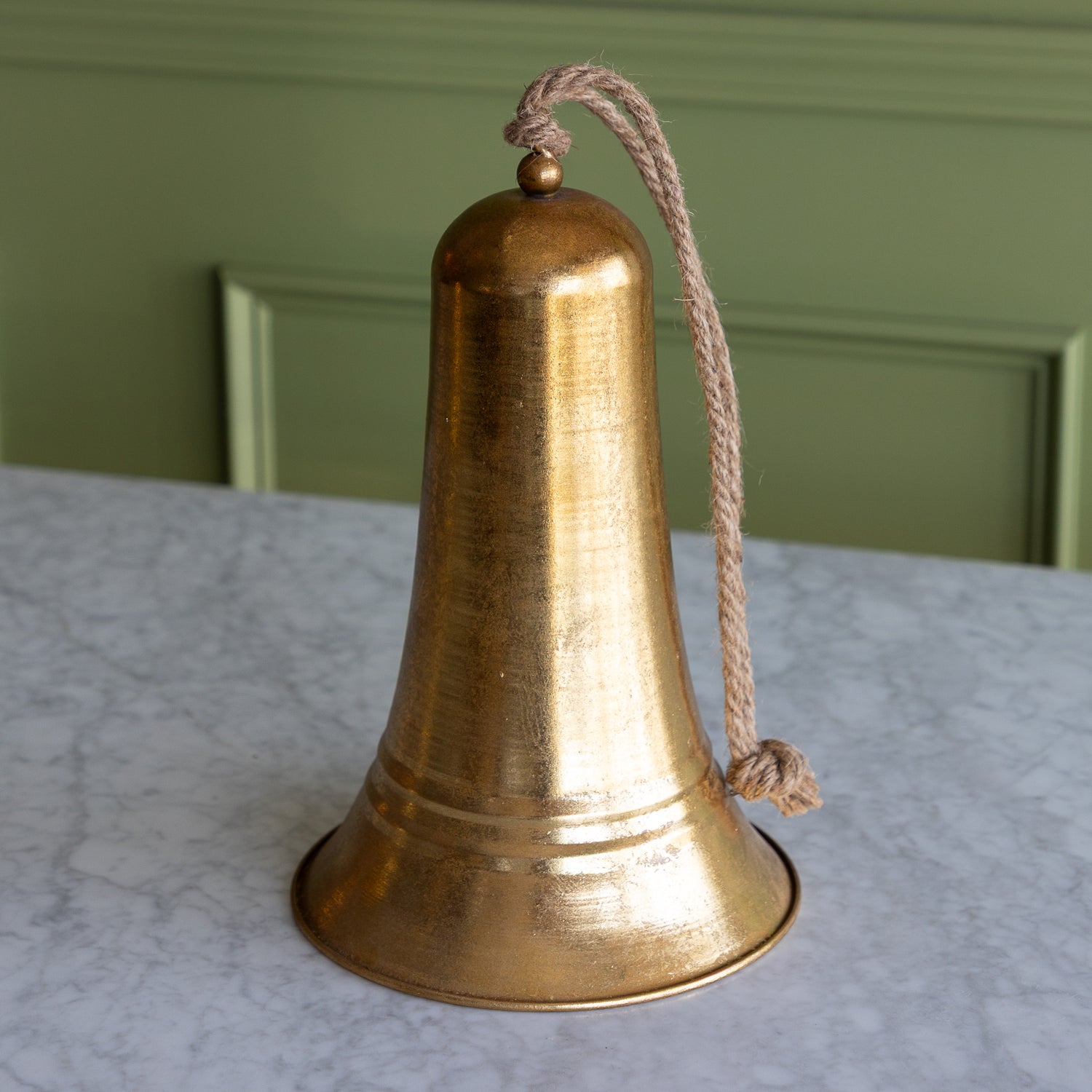 Bronze bell with a rope on a marble surface with a green wall background