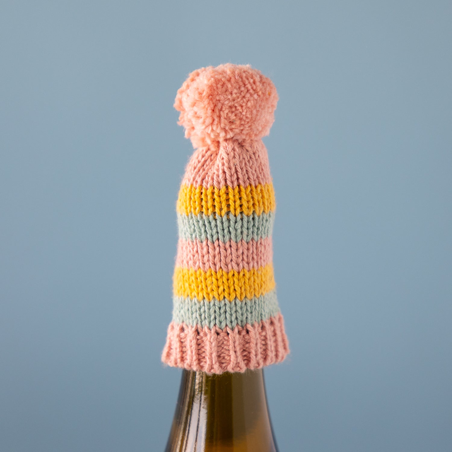 Knitted bottle cover with a pink pom-pom on a blue background.
