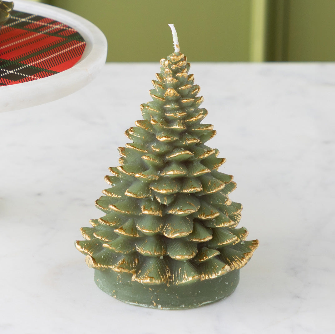 Green candle shaped like a Christmas tree with gold tips on a white surface.
