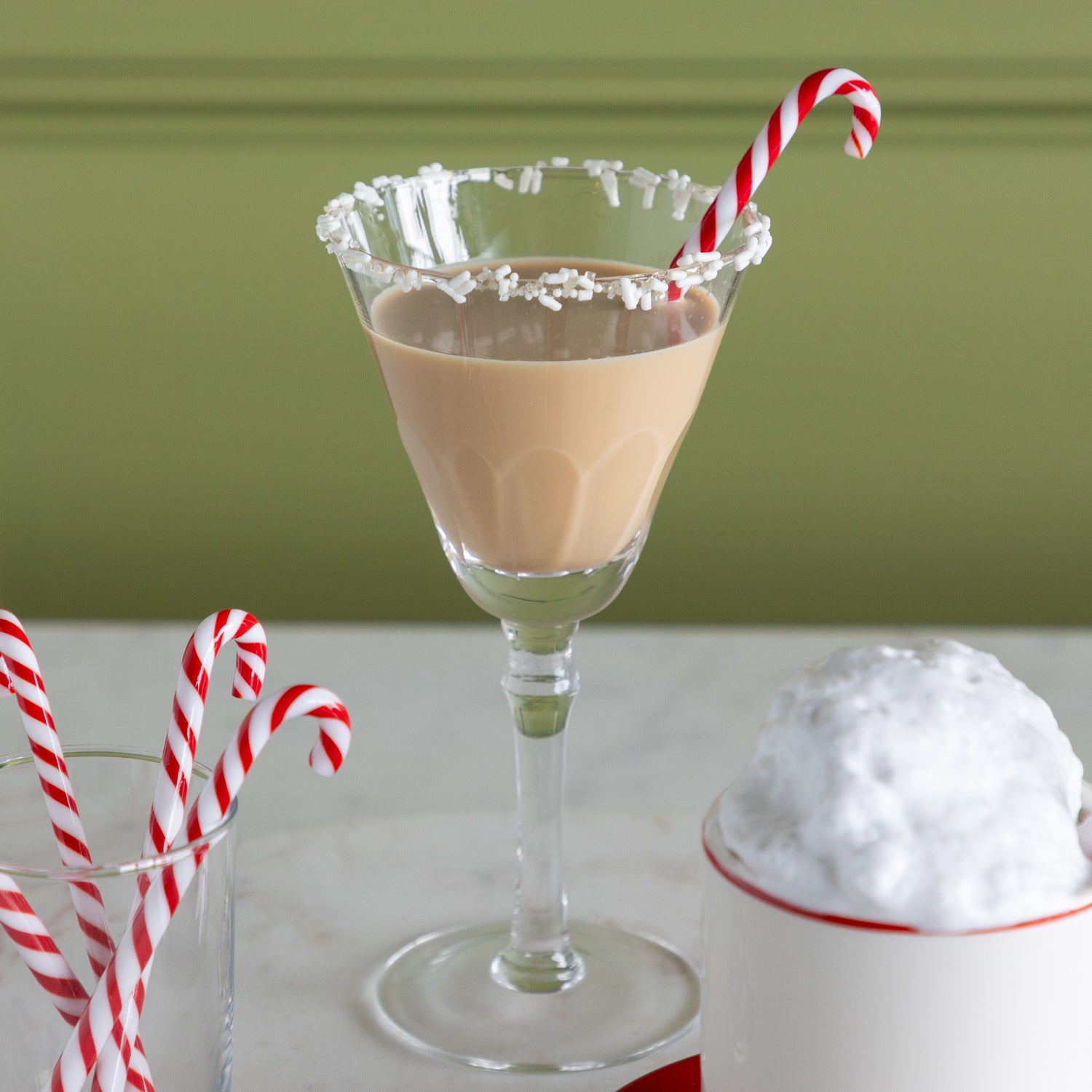 Mocha cocktail in a martini glass with a candy cane stir stick on a white surface.