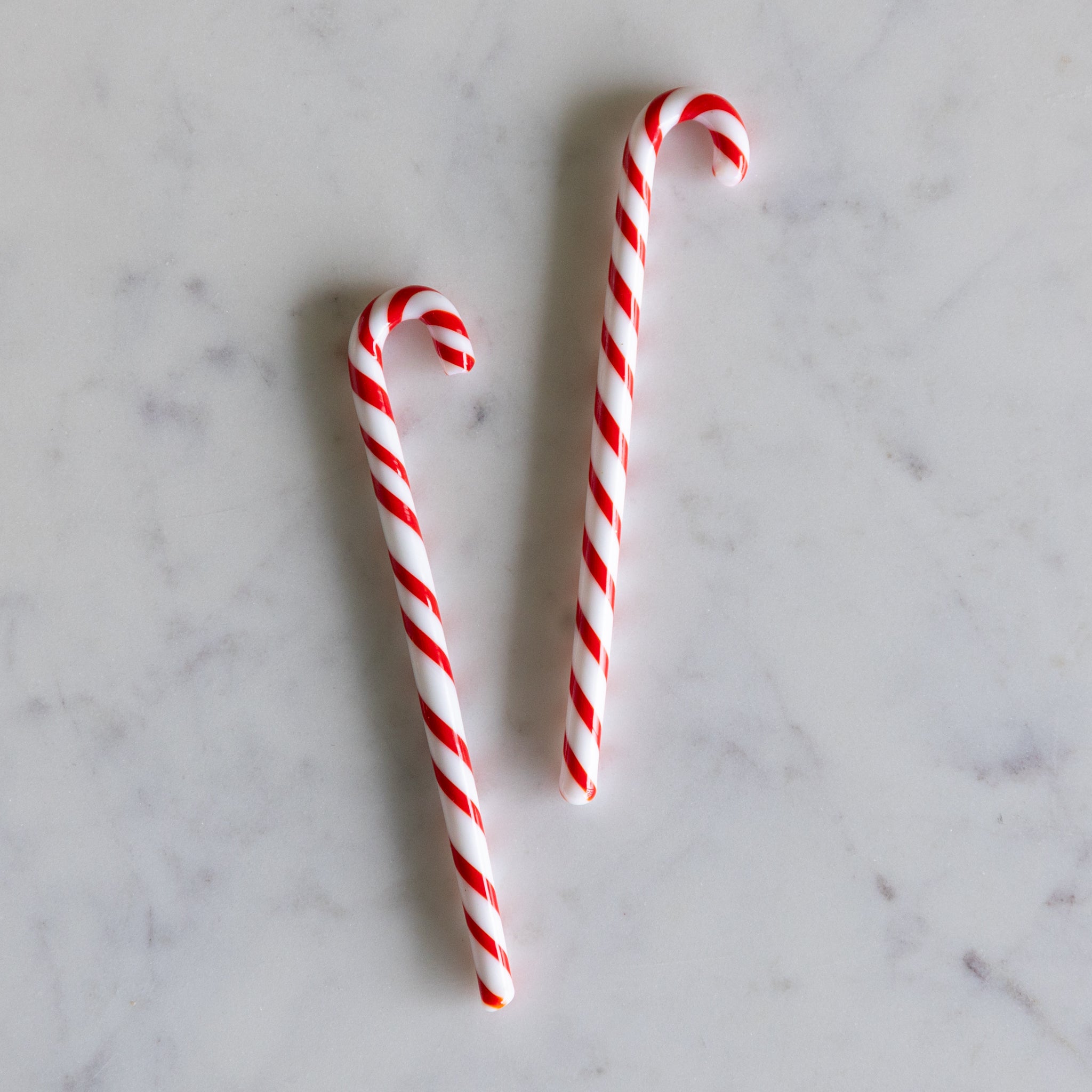 Two red and white striped candy cane stir sticks on a marble surface.